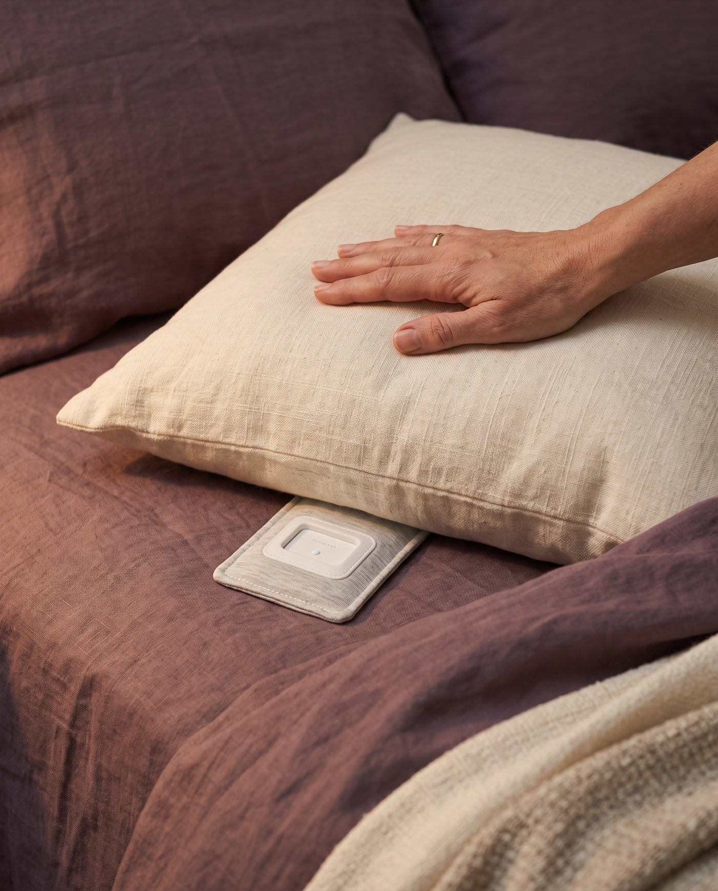 The Drowsie V3 speaker lying flat under a linen pillow on a made bed
